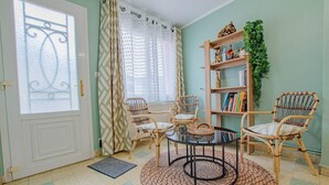 A room with a white door, two wicker chairs, a round table, a bookshelf, and a potted plant. - Les Bulles de l'Arce (BERTIGNOLLES)