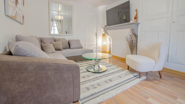 A living room with a sofa, a glass coffee table, a white armchair, a fireplace, and a mounted TV. - Les Bulles de l'Arce (BERTIGNOLLES)