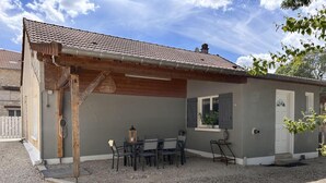 A small building with a tiled roof, a wooden pergola, and a gravel patio with outdoor seating. - Les Bulles de l'Arce (BERTIGNOLLES)