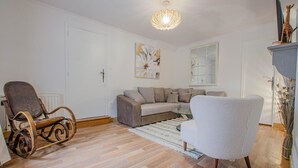 A living room with a sofa, two chairs, a glass coffee table, a wooden floor, a white door, a painting, and a ceiling light fixture. - Les Bulles de l'Arce (BERTIGNOLLES)