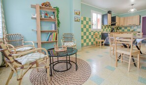 Cozy living space with a round table and wicker chairs, bookshelf, and kitchen area.