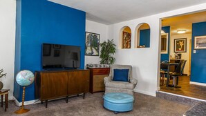 Un soggiorno con una parete blu, un mobiletto in legno, un poggiapiedi blu, un globo su un supporto e un televisore.