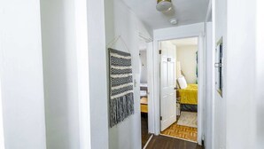 Un corridoio con un pannello decorativo a parete, un pavimento in legno e un letto con copripiumino giallo nella stanza adiacente.