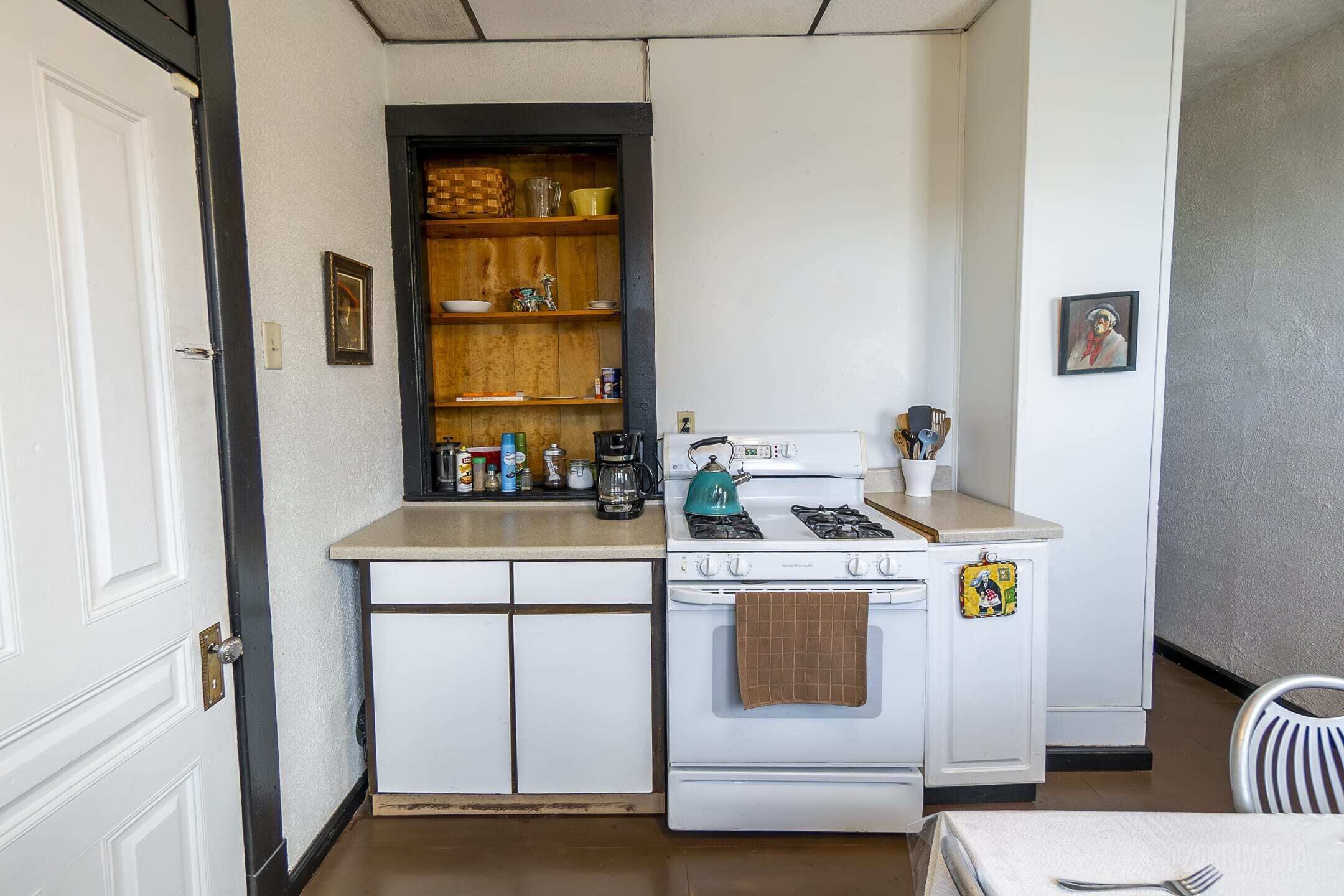 Een kleine keuken met witte keukenkastjes, een fornuis en een koffiezetapparaat.