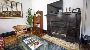 Un salon avec une cheminée, un téléviseur, une bibliothèque, un fauteuil en osier et une table basse en verre.