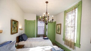 Une chambre d’hôtel avec deux lits, un lustre, des portes vertes et une fenêtre ornée de rideaux en dentelle.
