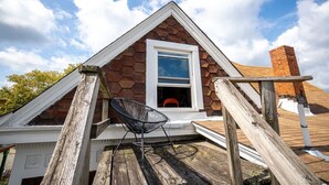 Ein Haus mit sechseckigem Dach, einem weißen Fenster und einer Holzterrasse mit einem Stuhl.
