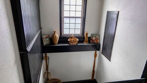 Eine schmale Treppe mit einem Fenster oben, eine Ablagefläche mit Dekorationen und ein Korb.