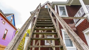 Eine Holztreppe führt zu einem Haus mit violetter Fassade und rotem Backstein.