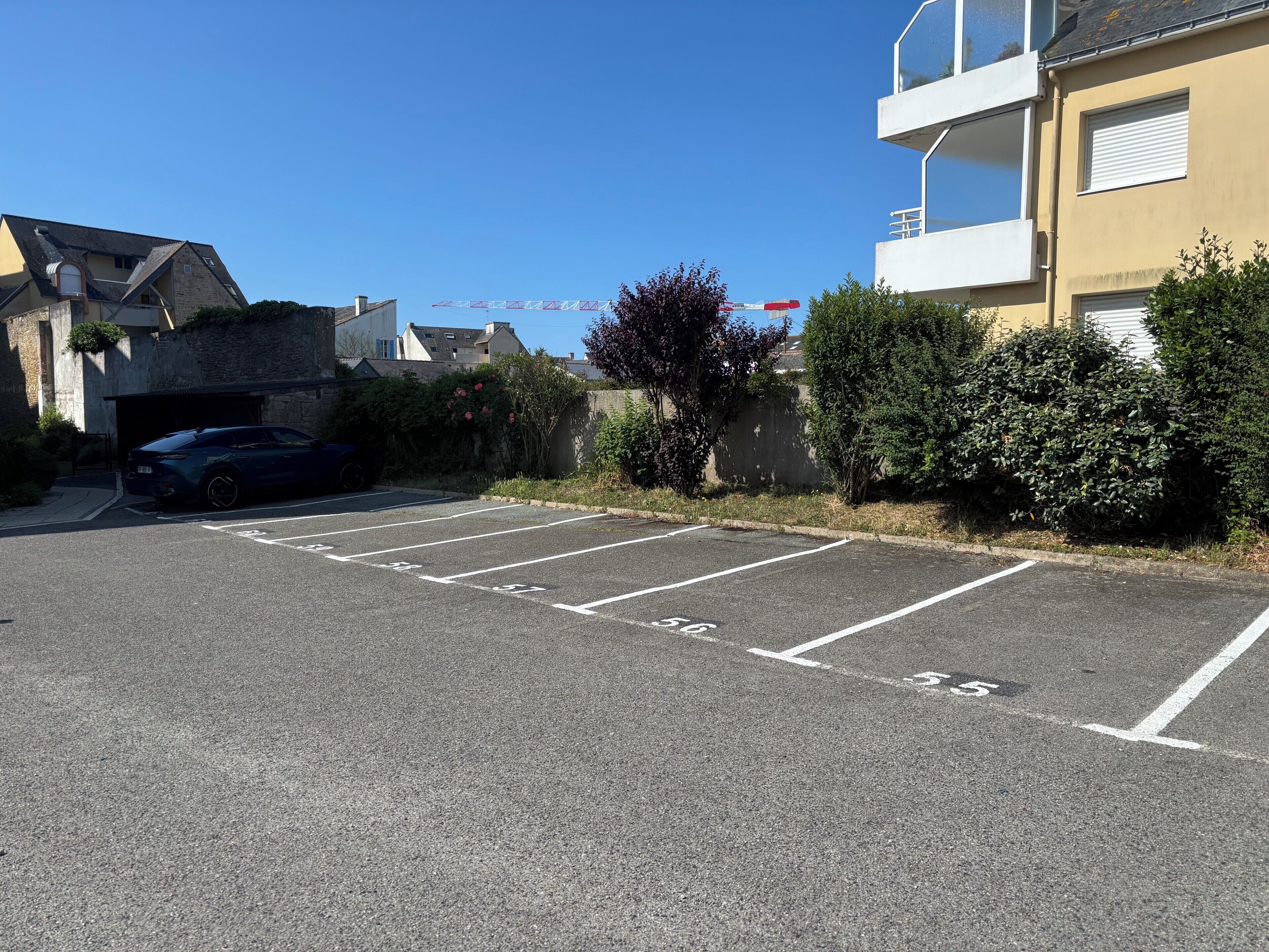 Un estacionamiento con espacios delimitados, un coche y un edificio con balcón.