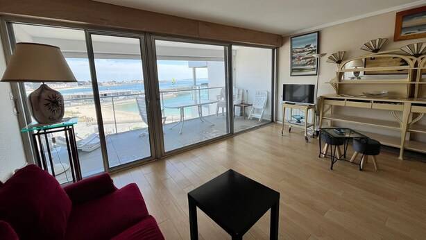 A spacious living room with a large sliding glass door leading to a balcony with a view of the sea.