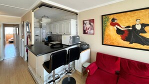 A compact living space with a kitchenette, a red sofa, and a painting on the wall.