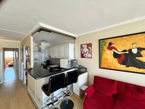Um espaço compacto para viver, com cozinha compacta, sofá vermelho e um quadro na parede.