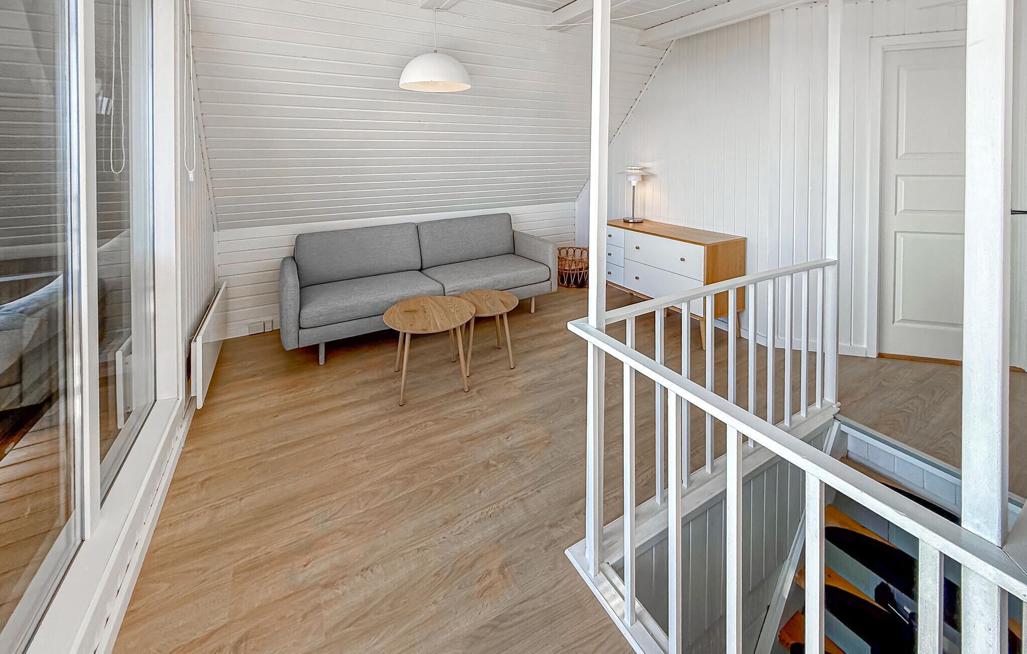 A room with a grey sofa, two small round tables, a white dresser, and a white railing.