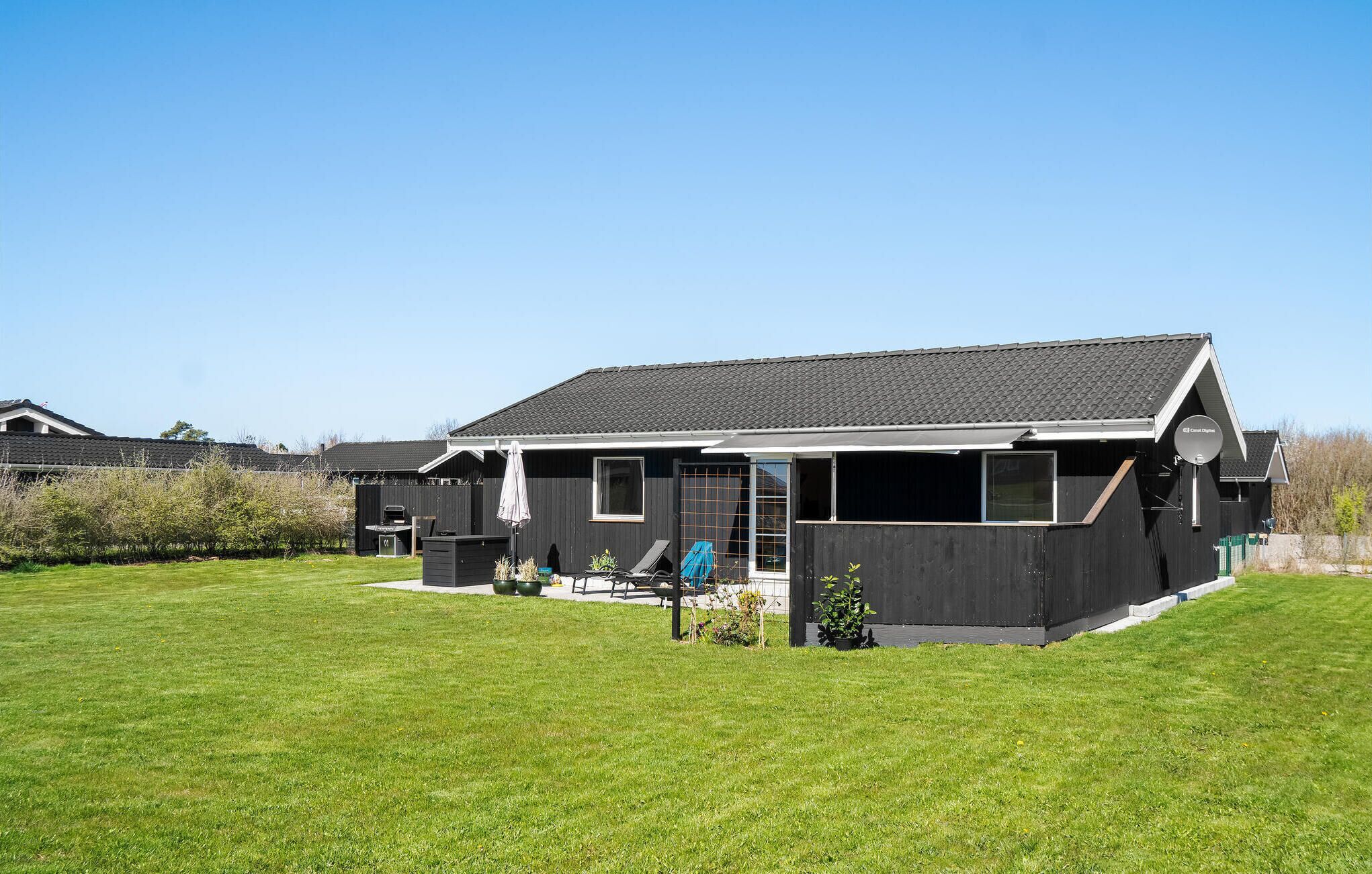 A modern house with a large lawn, a satellite dish, and a barbecue area.