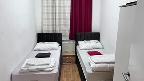 A small, narrow room with two single beds, a wooden floor, a white door, and a window with curtains. - Hostel Wieden (Vienna)