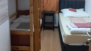A compact room with a bunk bed, a single bed, a small table, and a window with curtains. - Hostel Wieden (Vienna)