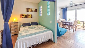 A bedroom with a bed, curtains, a bedside table, a lamp, wall art, and a balcony with a table and chairs. - Cozy apartment in Peníscola with house sea view (Peníscola)