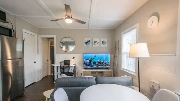 Una sala de estar moderna con una mesa de comedor, sofá, televisor y zona de cocina.