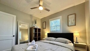 Ein Hotelzimmer mit Bett, Deckenventilator, Fenster mit Jalousien, Nachttisch mit Lampe und Schrank.
