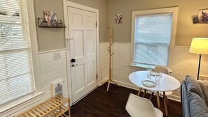 A room with a dining table, two chairs, a bench, a door, and a window with blinds. - The Red Door Cottage (Hendersonville)