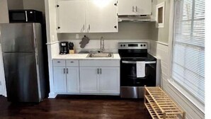 A compact kitchen with white cabinets, a stainless steel refrigerator, a stove, and a wooden bench. - The Red Door Cottage (Hendersonville)