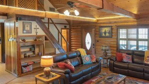 A spacious log cabin interior with a large leather sofa, a wooden staircase, and a large clock on the wall.