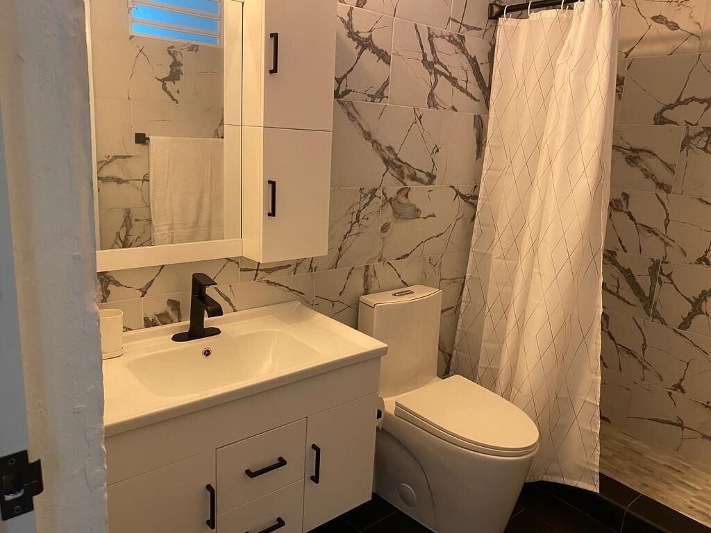 A bathroom with a white sink, black faucet, white toilet, and a marble-patterned wall.