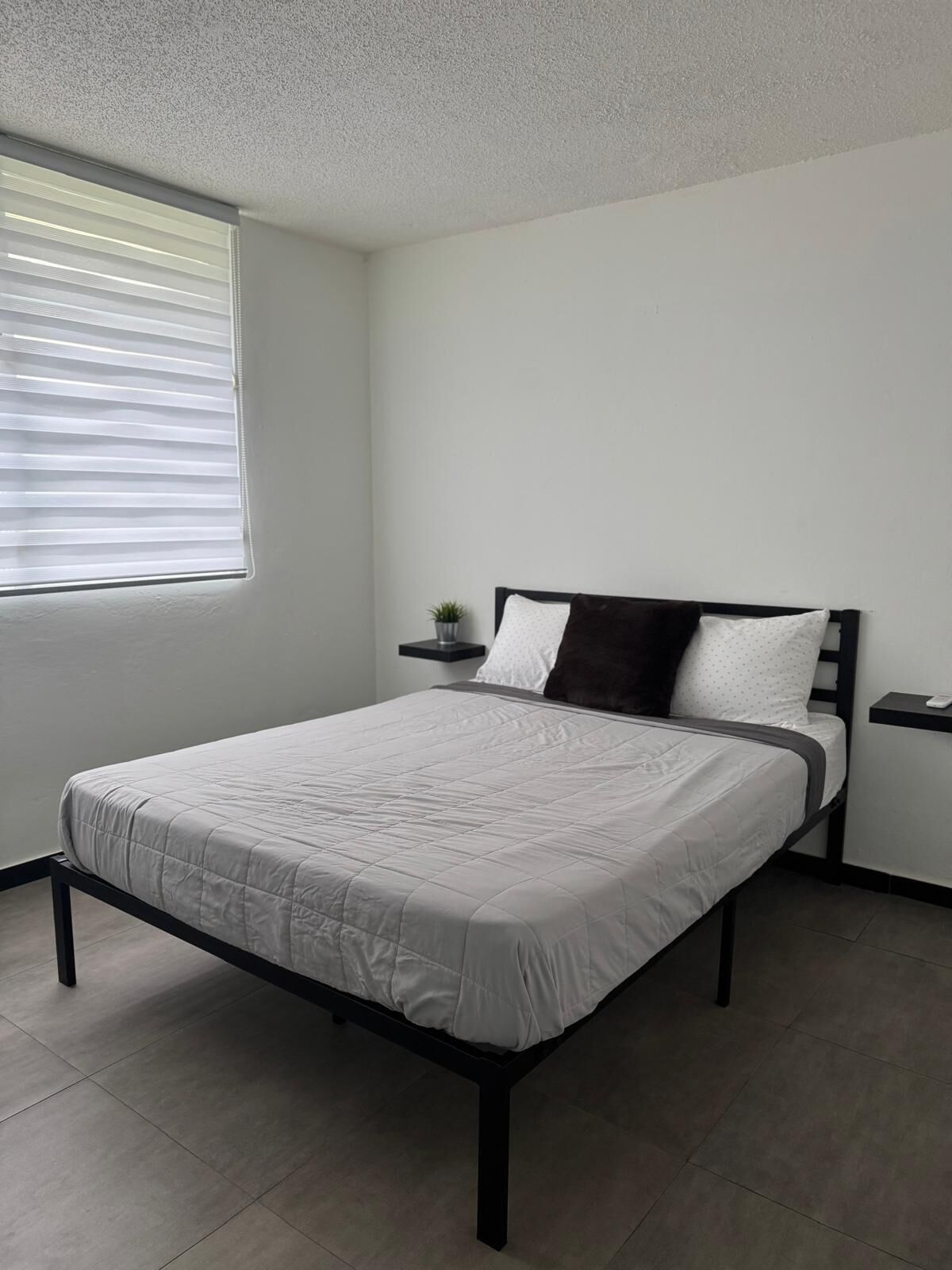 A neatly arranged bedroom with a bed, a nightstand, and a window with blinds.