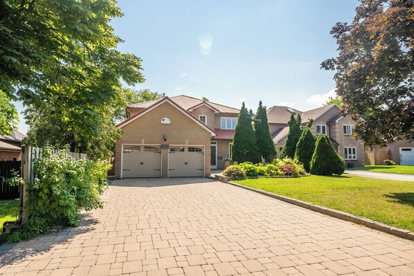Une allée menant à une maison avec deux garages, entourée de verdure et d’une pelouse bien entretenue.