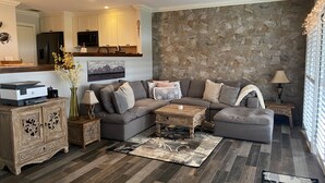 Una sala de estar moderna con una pared de acento de piedra, un sofá seccional gris, una mesa de centro de madera y una alfombra decorativa.