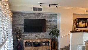 Una sala de estar con piso de madera, un televisor de pantalla plana montado en la pared, una consola con una planta y una escalera que sube a otro nivel.