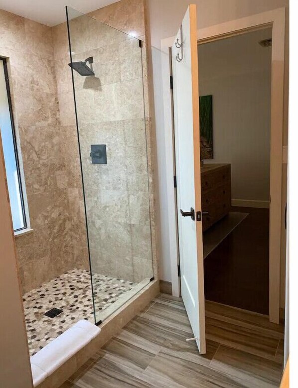 A glass-enclosed shower with a tiled floor, a wooden door, and a small window.