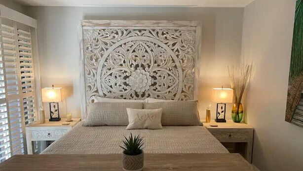 Un dormitorio con una cama grande, dos mesitas de noche, un cabecero decorativo y una mesita con una lámpara.