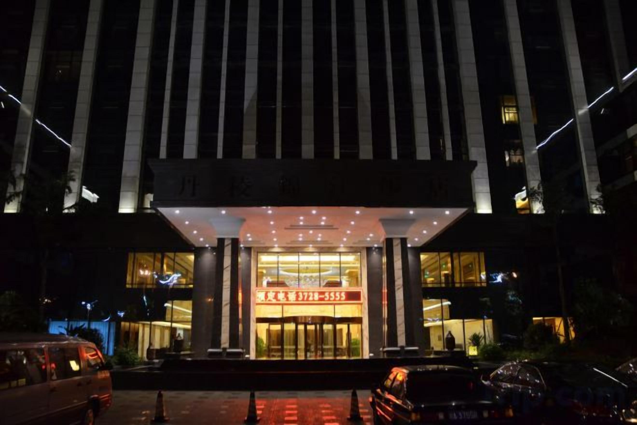 Een hotel ingang met een grote verlichte reclame, een overdekte entree en een parkeerplaats.
