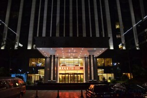 A hotel entrance with a large illuminated sign, a covered entrance area, and a parking lot.