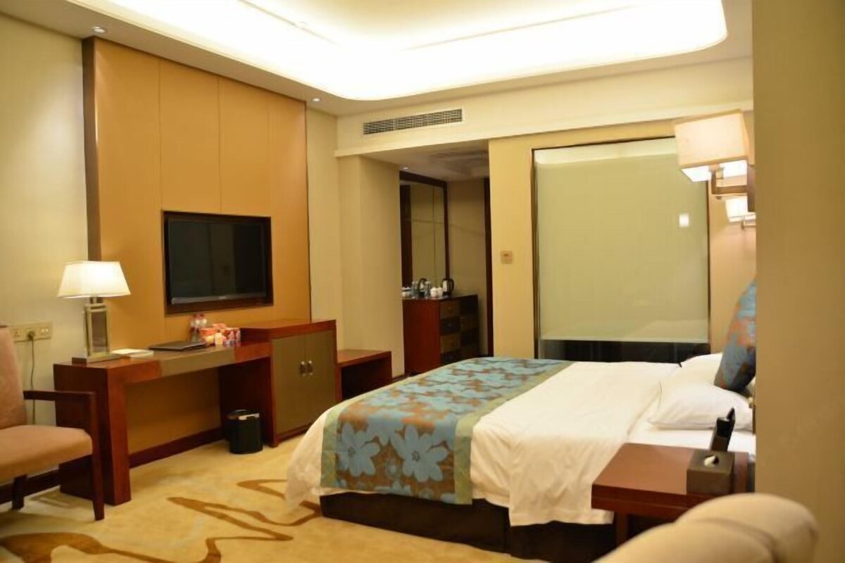 A hotel room with a bed, a desk, a chair, a TV, and a mirror.