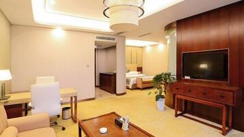 A hotel room with a television, a desk with a lamp, a sofa, a coffee table, and a bed.