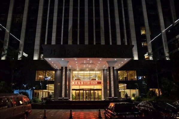 A hotel entrance with a large sign, a covered entrance area, and a parking lot.