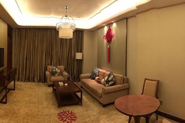 Un salón de hotel con sofá, sillones, una mesa de centro, televisor y candelabro.
