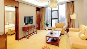 A hotel room with a bed, a TV, a sofa, a coffee table, and a large window with curtains.
