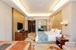 Una habitación de hotel con cama, mesita de noche, lámpara, televisor y escritorio con silla.