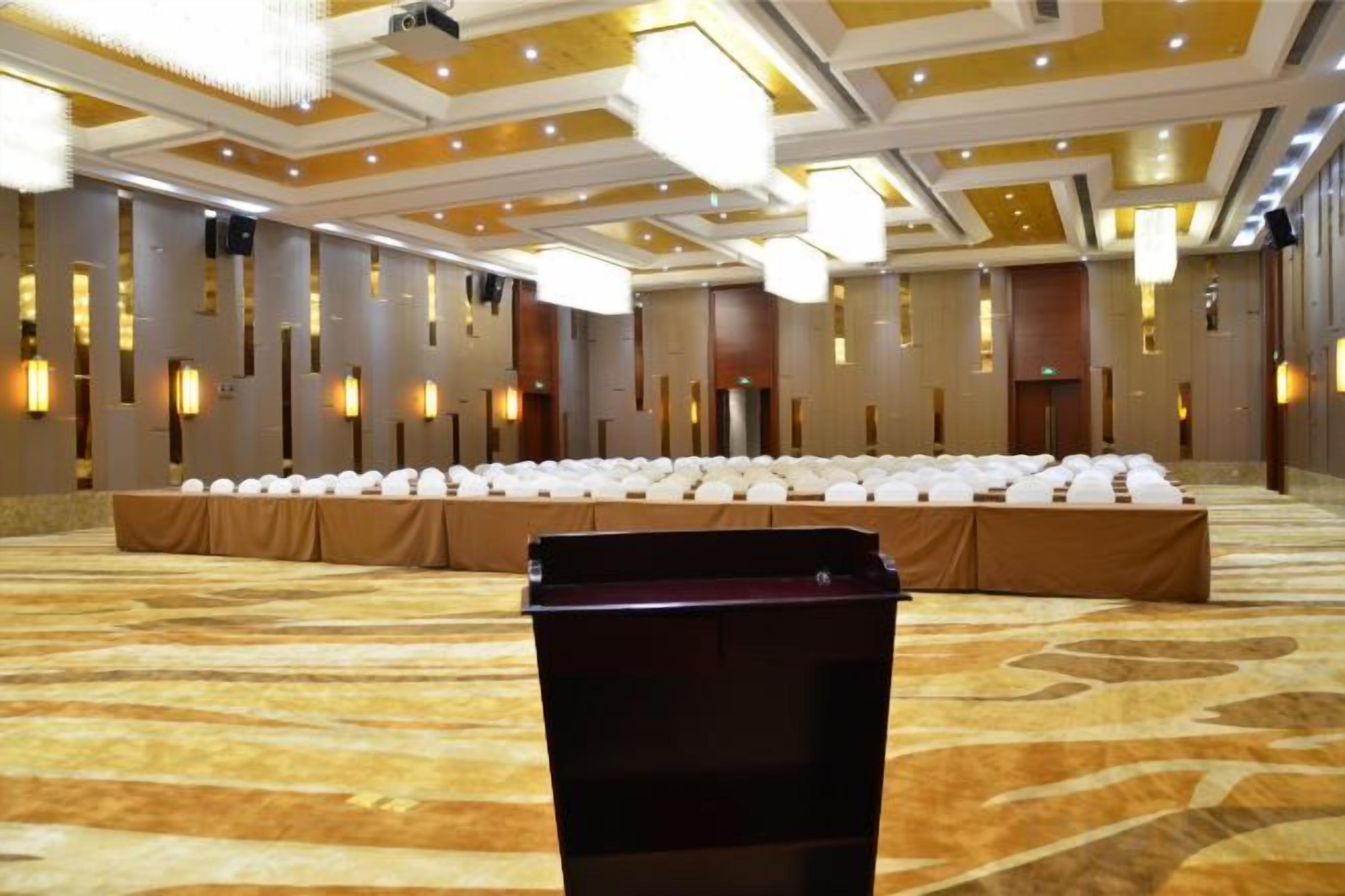A conference room with a long table covered in white chairs, a podium, and a carpeted floor.
