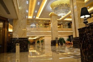 A spacious lobby with marble flooring, a grand chandelier, and a high ceiling.