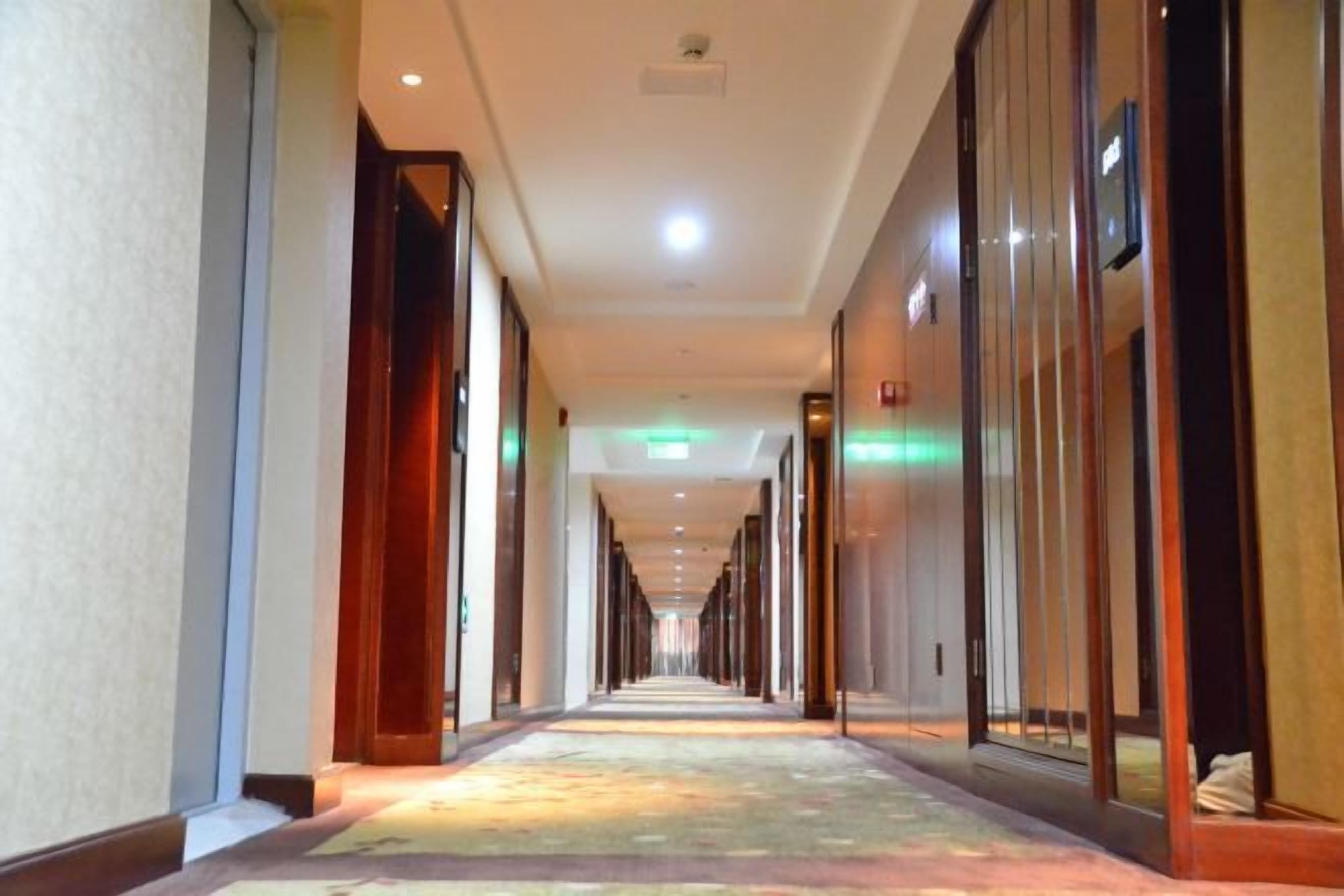 A long, narrow hotel corridor with doors on both sides, recessed lighting, and a patterned carpet.