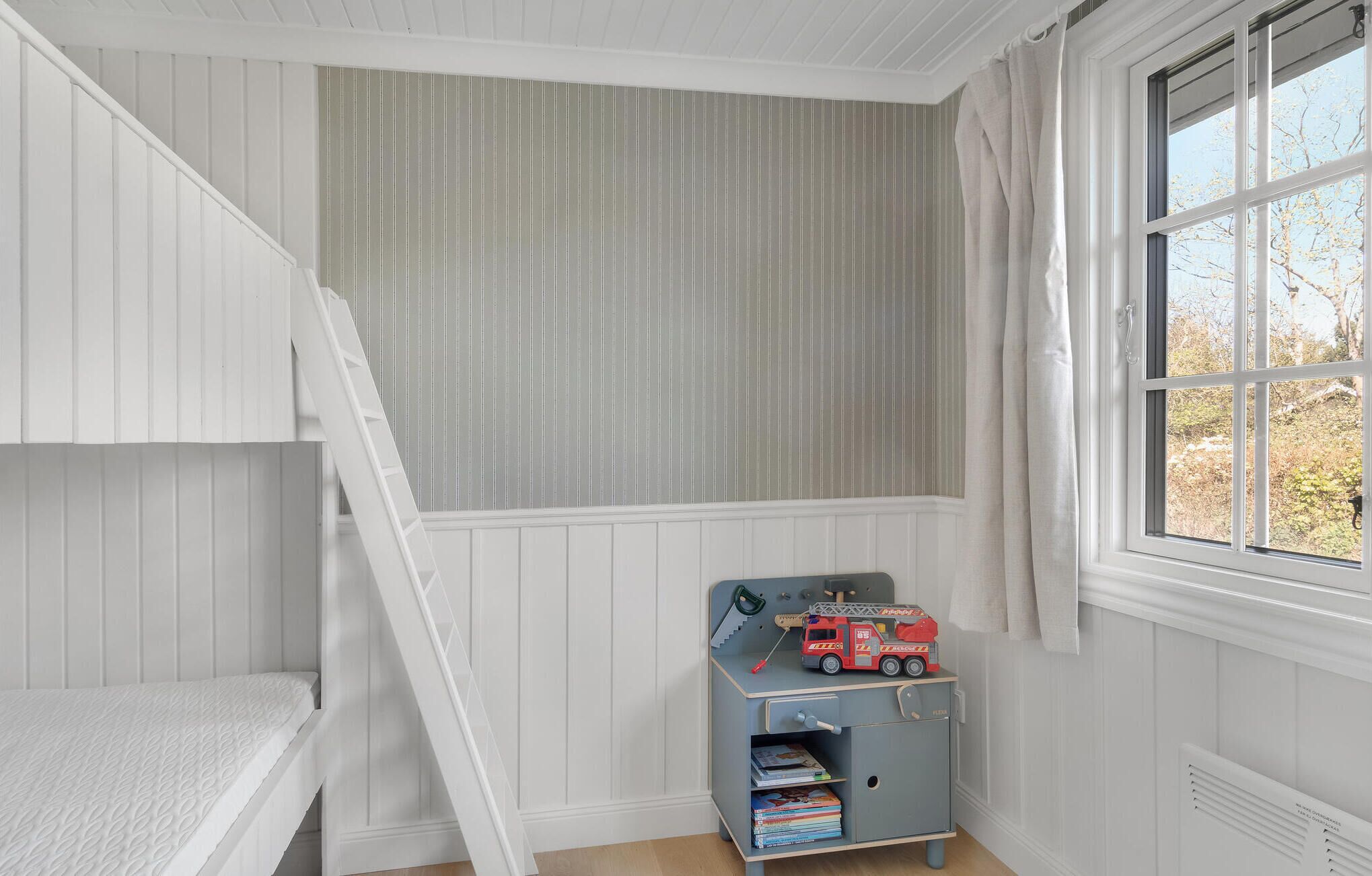 Un dormitorio infantil con literas, una ventana con cortinas y un camión de bomberos de juguete sobre una estantería.