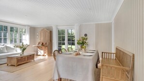 Comedor con una mesa preparada para cuatro, un banco de madera, un armario y vistas al exterior a través de ventanas amplias.