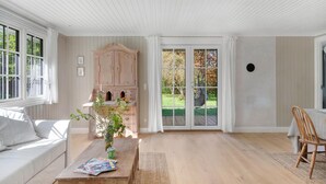 Una habitación luminosa y bien iluminada, con techo blanco, un armario de madera, una mesa de comedor con sillas y un amplio ventanal con cortinas.
