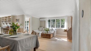 Una habitación amplia con zona de comedor, sofá y ventana con cortinas.