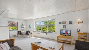 Una sala de estar moderna con comedor, ventanas amplias, televisor y una mesa de centro de madera.